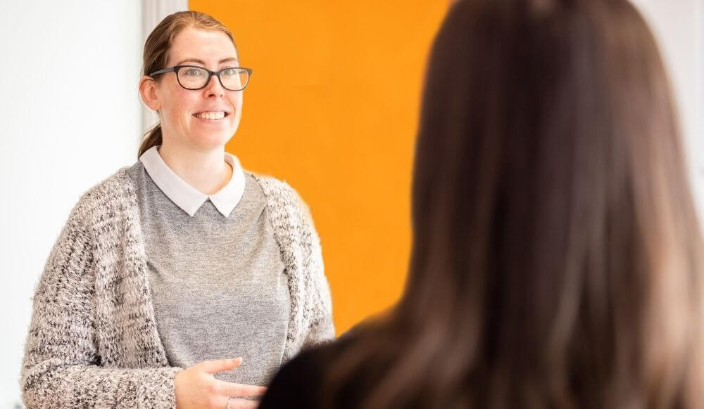 Woman smiling and talking to a young woman who has the back of her head to the camera