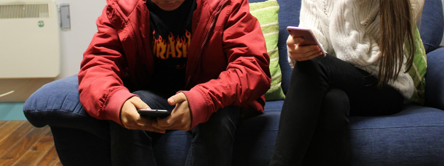 Close up of two people using their phones sitting on a couch