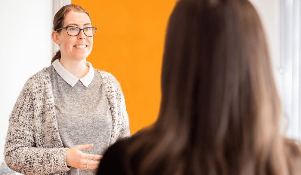 Woman talking to young woman who has back of her head to the camera