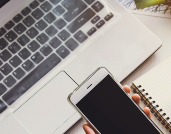 Picture of a hand holding a mobile phone over a laptop