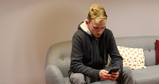 Picture of a young man sitting down looking at his phone