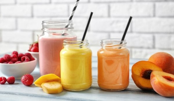 Three smoothies in jars with straws sitting on a counter