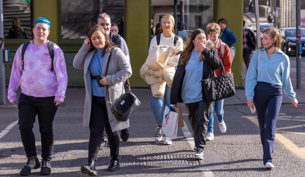 Seven young people cross the road together.