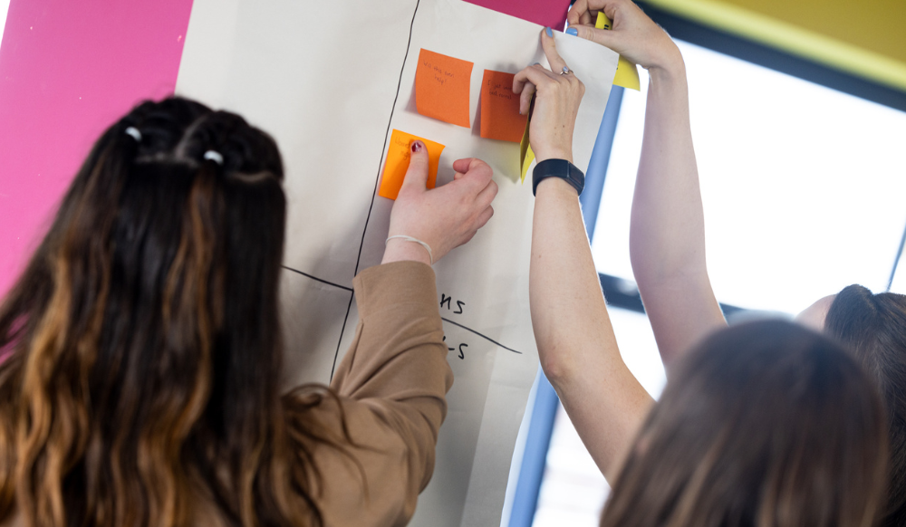 Two people sticking post-it notes to a wall, brainstorming