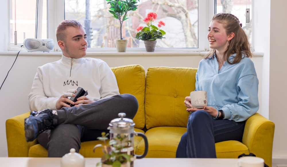 Two young people sitting on a couch, smiling and talking