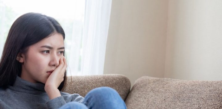 Dark haired girl sitting on couch looking out into the distance looking sad