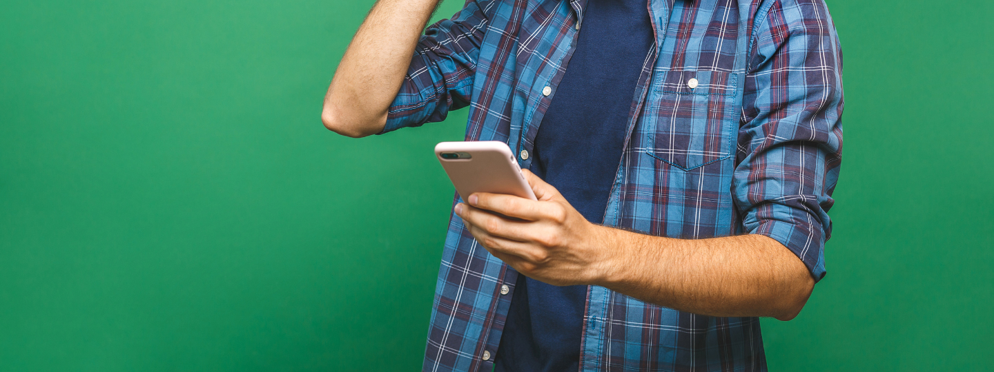 man's midriff holding a phone beside a laptop