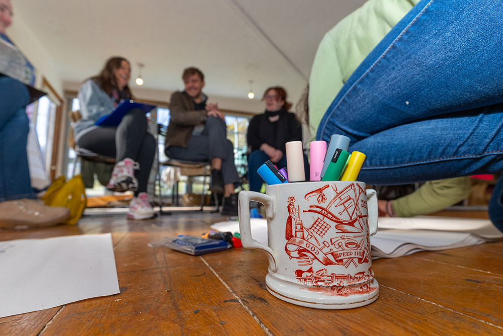 cup filled with markers with young people sitting blurred in the background